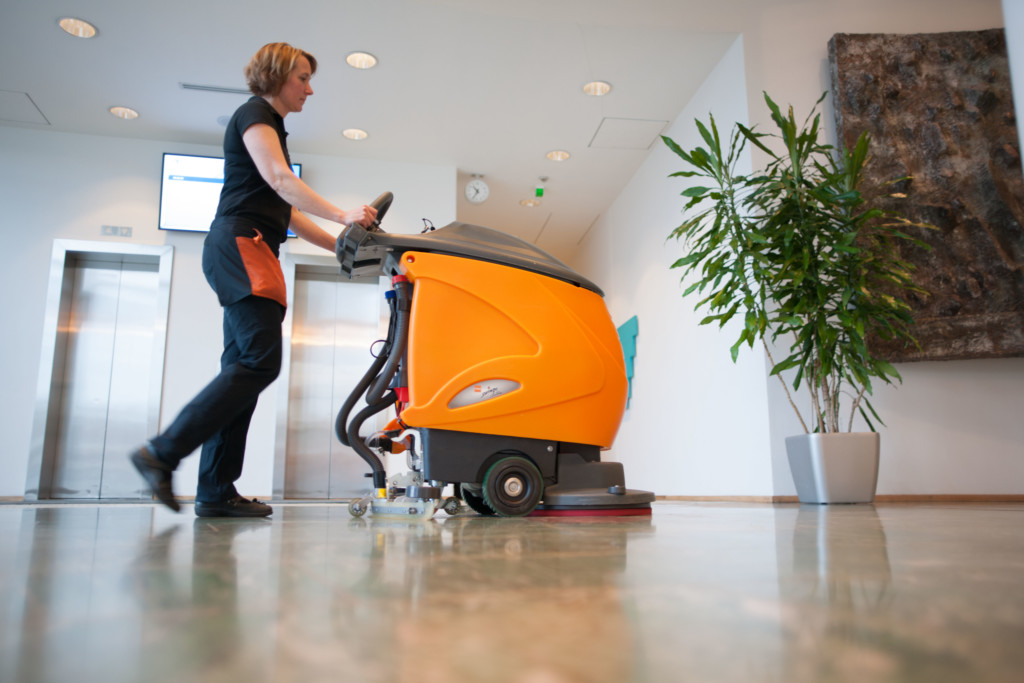 A cleaner is washing the floor with a floor cleaning machine.
