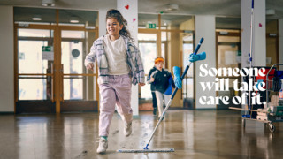 A secondary-school-aged child is running in a bright school hallway, with another child in the background. Someone is wiping the floor with a cleaning mop, but only the glove-covered hands of the cleaner holding the mop are visible. The text in the lower left corner reads "Someone will take care of it." A lifestyle image.