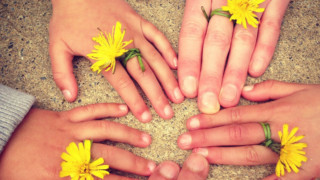 Hands of children and adults wearing flower rings.