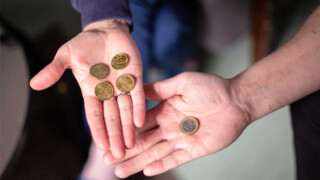 Two hands. One hand holds four coins, and the other holds one euro.