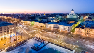 Ett flygfoto av vintriga Helsingfors centrum vid skymningsdags, en blå himmel, gula ljus, domkyrkan syns i bakgrunden.