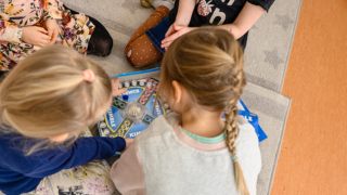 Day care-aged children playing Kimble on a carpet, the child in the front has her hair tied back in a plait.