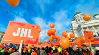 JHL:n lakkokyltti ja paljon ihmisiä Helsingin Senaatintorilla, taustalla Tuomiokirkko. Aurinkoinen päivä, taivaalla vaaleita pilviä.