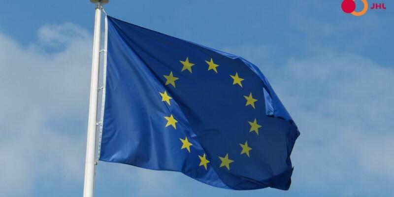 Euroopan Unionin lippu liehuu sinistä taivasta vasten. Oikeassa yläkulmassa ammattiliitto JHL:n logo.