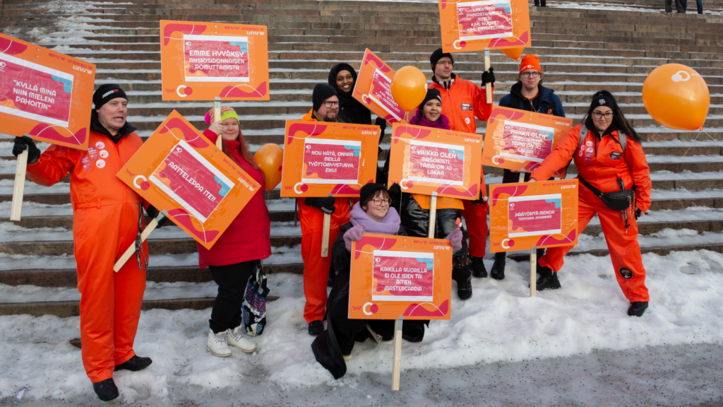 Ammattiliitto JHL nuoret ja opiskelijat oranssit opiskelijahaalarit päällä Stop nyt! -mielenosoituksessa helmikuussa 2024.