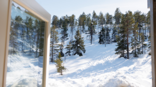 An open cabin window with a view to a sunny, snow-covered slope