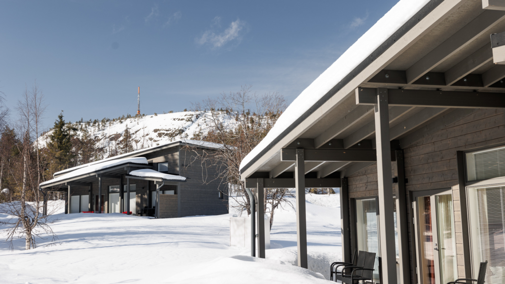 Two new dark grey holiday houses with large windows in a snowy winter landscape at Ruka.