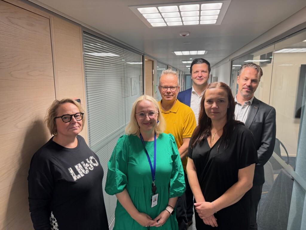 Vaihtoehtoinen teksti: A group photo where the negotiators of the collective agreement for the private early childhood education and care sector are standing in an office corridor.