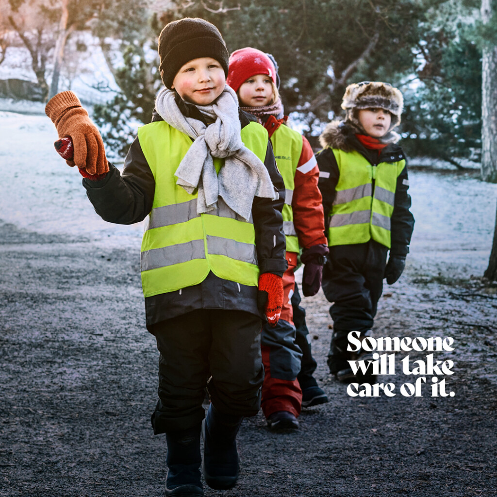 Day care aged children are walking in a snowy landscape, led by an adult. Only the glove-covered hand of the adult is visible. The text on the image reads "Someone will take care of it."